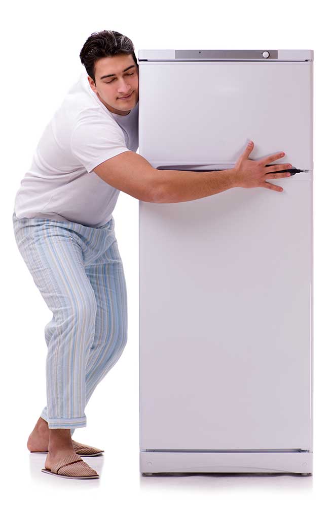 A man leaning against a refrigerator with his hand on the door.