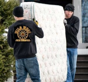 Two men moving a mattress on top of the ground.