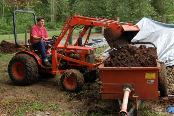 A man on a tractor pulling a trailer full of dirt.